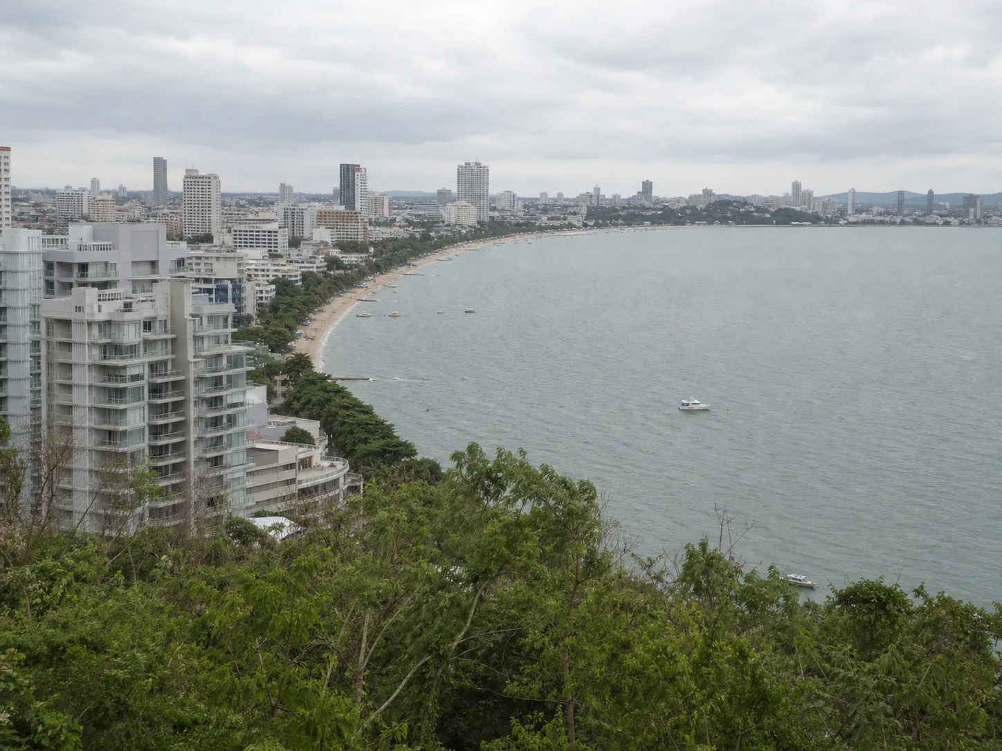 The curve of Pattaya Bay seen from the Pratumnak headland in flat daylight, mid-rise condos along the shore