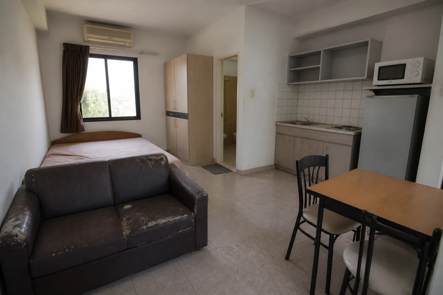 A small furnished studio rental with a kitchenette, a small table and a worn two-seat sofa