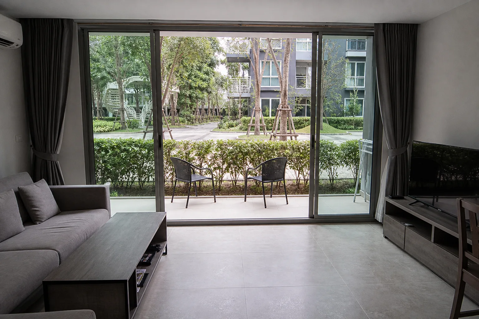 A ground-floor one-bedroom condo opening onto a paved terrace beside a garden walkway