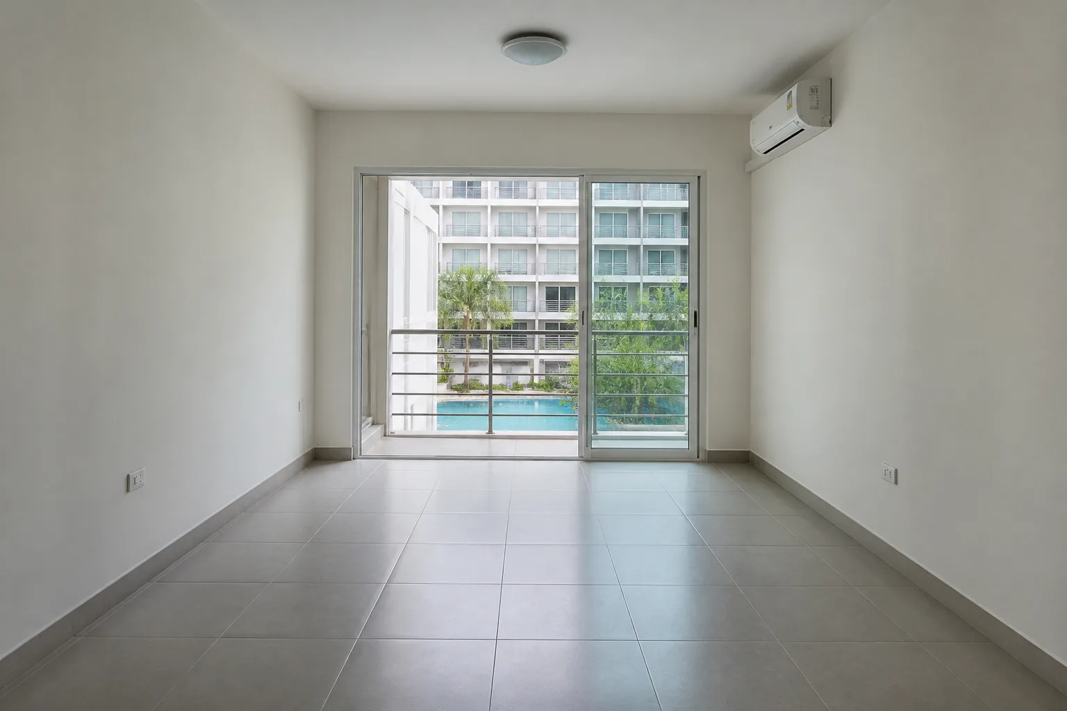An empty unfurnished one-bedroom condo with bare tiled floors and a balcony overlooking a pool deck