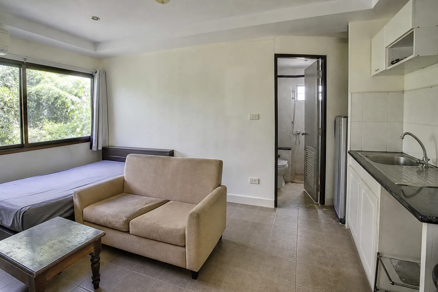 A small furnished studio in an older condo building, garden view through a single window