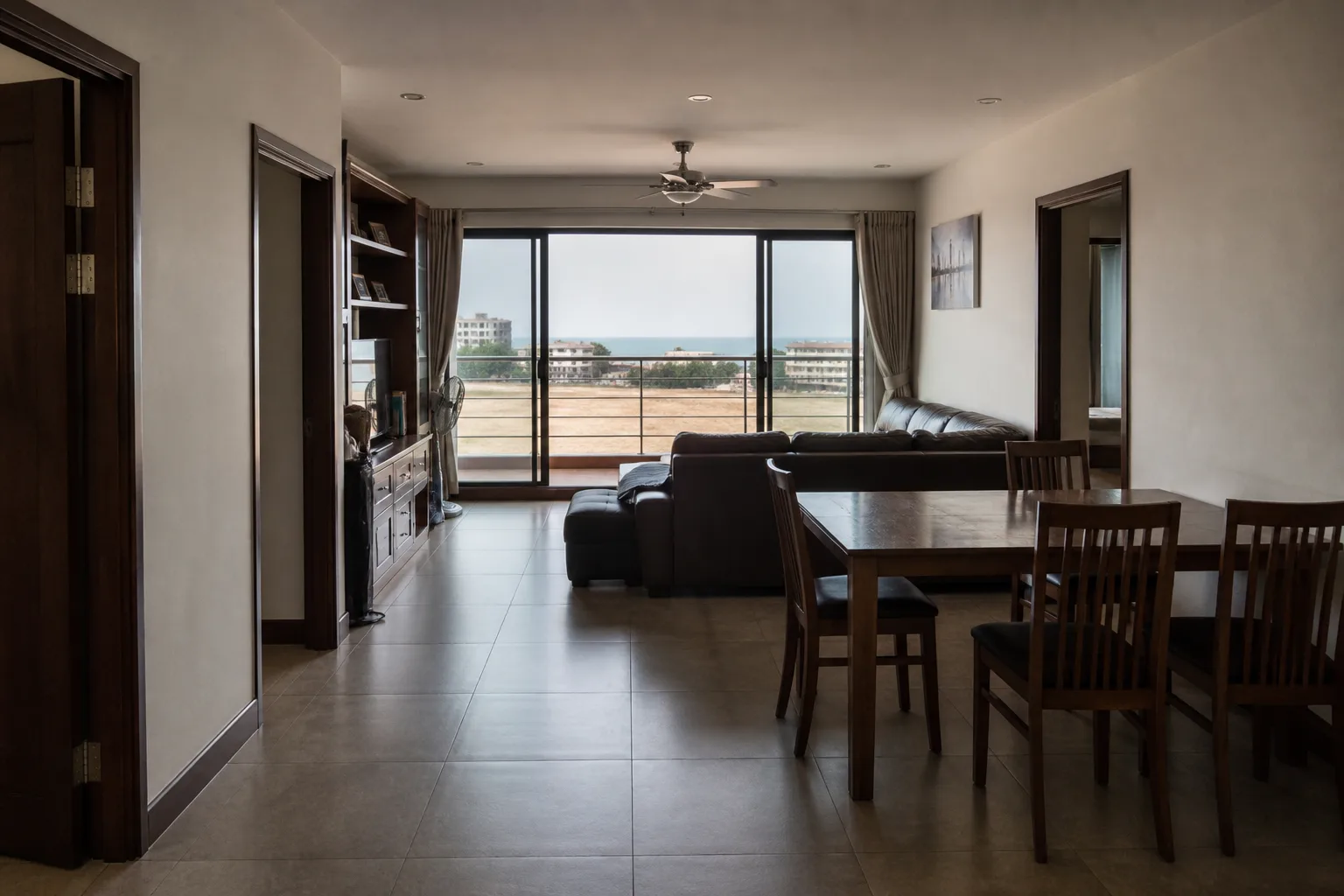 A two-bedroom condo living and dining area with a wide balcony and a partial sea view over low rooftops
